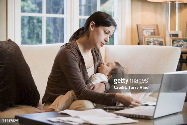 hispanic woman paying bills online with sleeping baby - houston texas home stock pictures, royalty-free photos & images