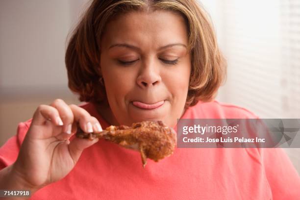 middle-aged overweight hispanic woman licking her lips and looking at a piece of fried chicken - eating chicken stock-fotos und bilder