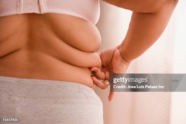 overweight woman pinching a roll of fat on her side - overgewicht stockfoto's en -beelden