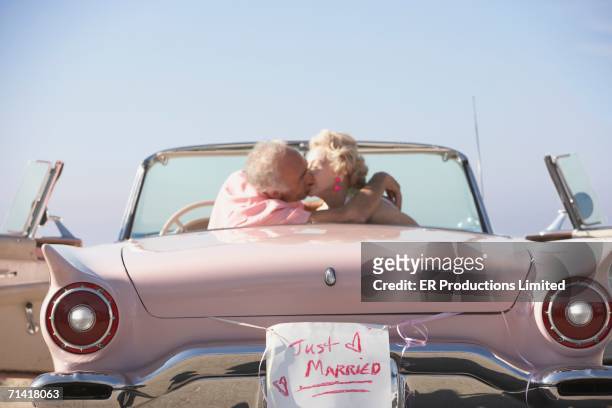 senior couple kissing in pink convertible with just married sign - just married car stockfoto's en -beelden