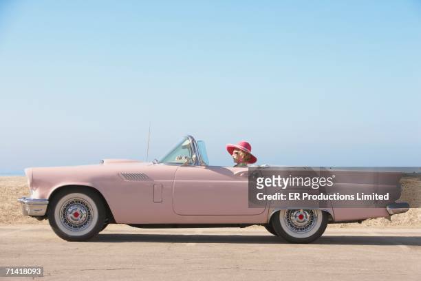 senior woman driving pink convertible - vista laterale foto e immagini stock