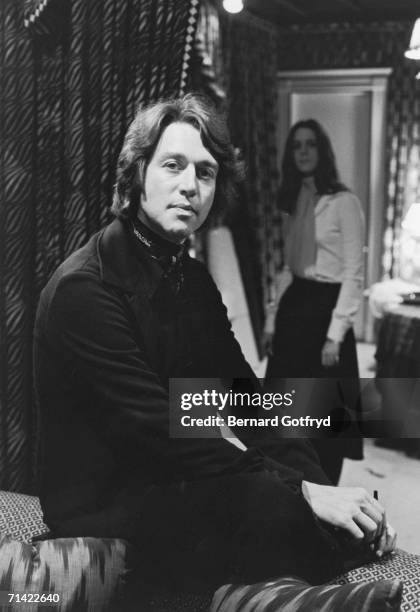 American fashion designer Halston poses for a portrait as he sits on the back of a couch, an unidentified woman stands in the background, 1970....