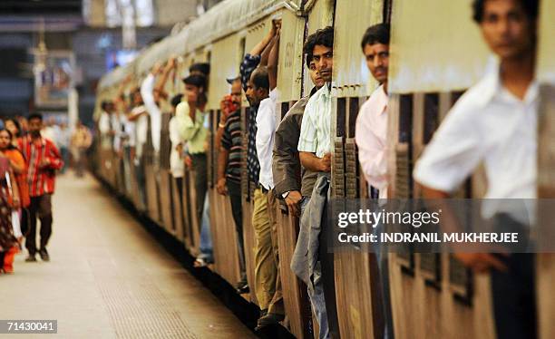 Commuters stand in the doorways of a crowded local train as it leaves Churchgate railway station in Mumbai, 13 July 2006. The death toll from a wave...