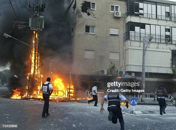 Israeli policemen rush to the scene of a burning electricity pylon and damaged building moments after a volley of Hezbollah Katyusha rockets struck...