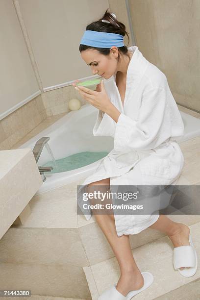 side profile of a young woman sitting near a bathtub and smelling a dish of bath crystals - crystal slipper stock pictures, royalty-free photos & images