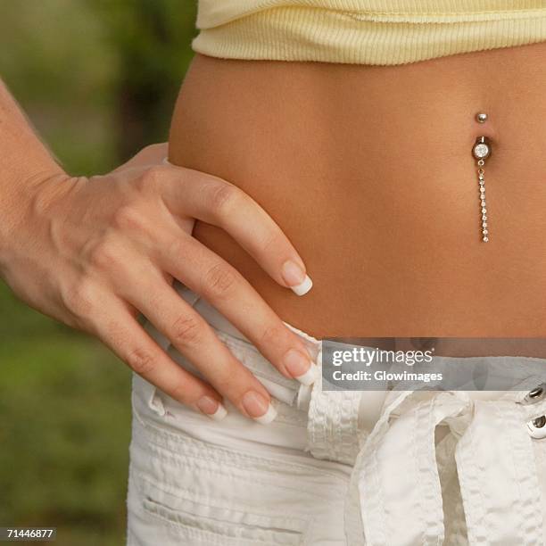 mid section view of a woman with her hand on her hip and showing her pierced belly button - belly button piercing foto e immagini stock
