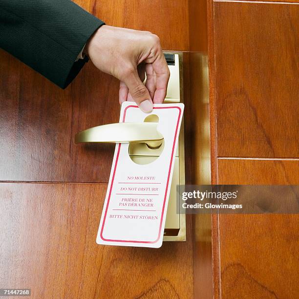 close-up of a person's hand hanging a do not disturb sign on a door knob - handle stock-fotos und bilder