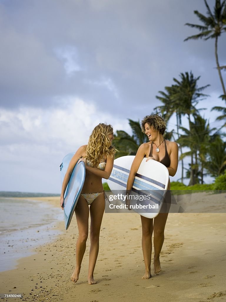 Two young women holding surfboards and walking on the beach