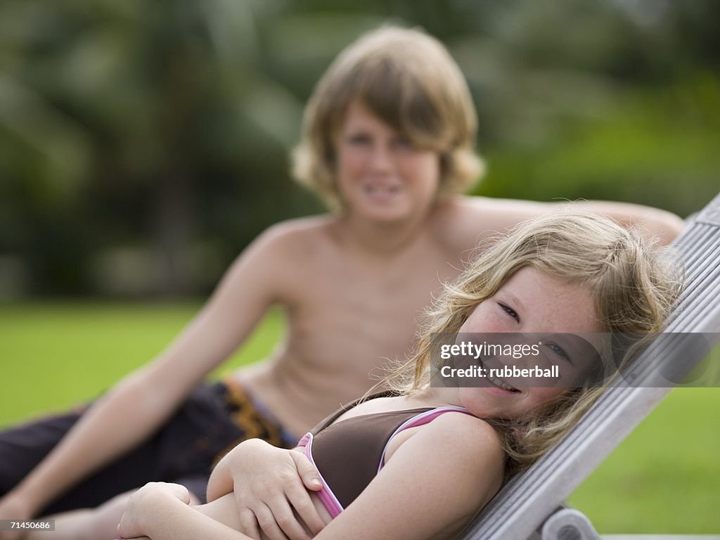 Portrait of a girl reclining on a lounge chair with her brother behind her