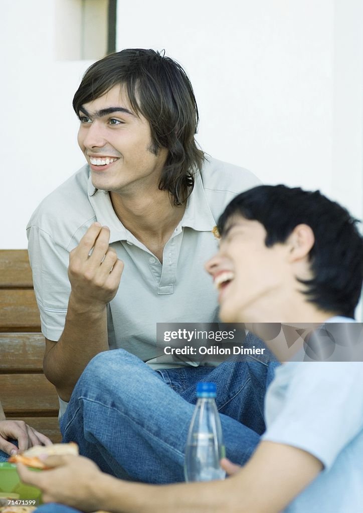 Two young adult friends with refreshments, laughing