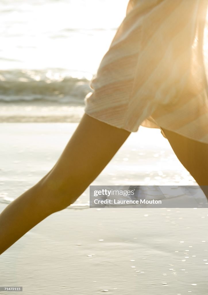 Woman walking on beach, mid section