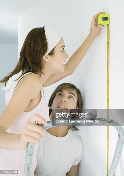 woman on ladder using measuring tape as man watches - woman measuring tape stock pictures, royalty-free photos & images