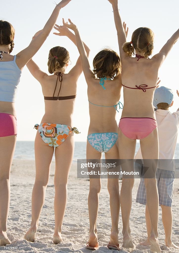 Group of kids waving on beach, rear view