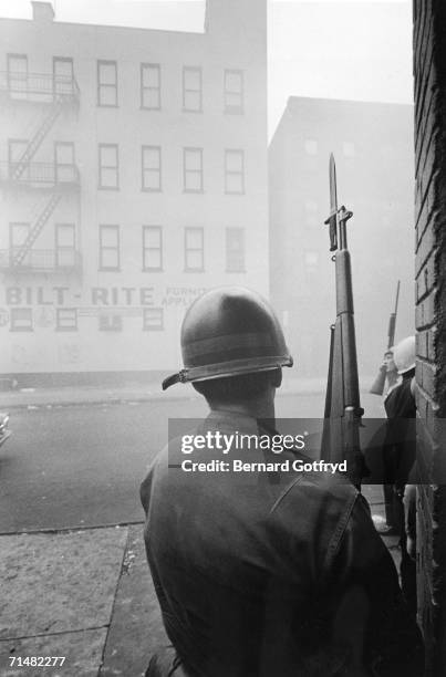 National Guardsman stands behind a corner and holds a Garand rifle with fixed bayonet during the suppression of riots, Newark, New Jersey, July 1967....