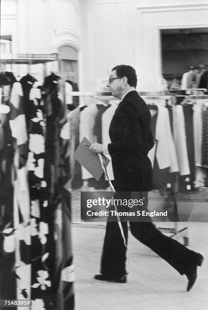 American fashion designer James Galanos walks past racks of clothing in a Saks Fifth Avenue department store, a notepad and a tape measure in his...