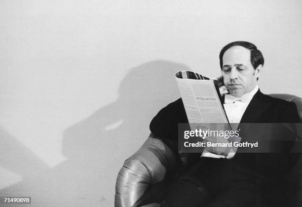 Portrait of French conductor and composer Pierre Boulez, dressed in a tuxedo, who sits in a chair and reads a music magazine, 1960s or 1970s.
