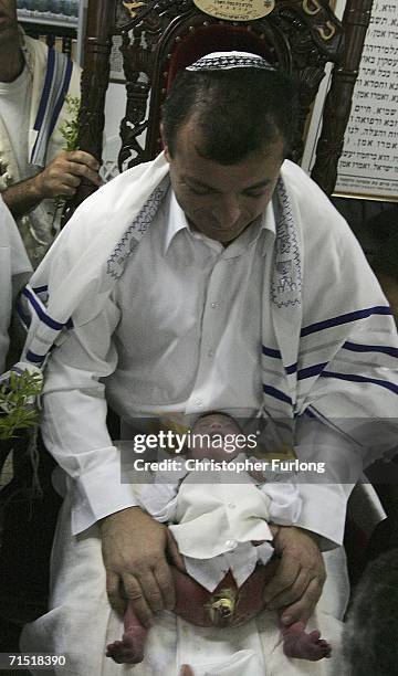 The godfather of eight-day-old Ofir Hen holds him whilst he is circumcised by the local Rabbi inside a bomb shelter on July 26, 2006 in Haifa,...