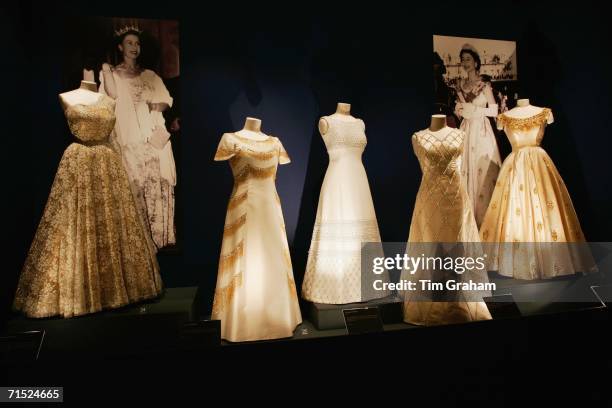 Beaded and embroidered white and gold evening dresses designed by Sir Norman Hartnell for Queen Elizabeth II stand on display at an exhibition of her...