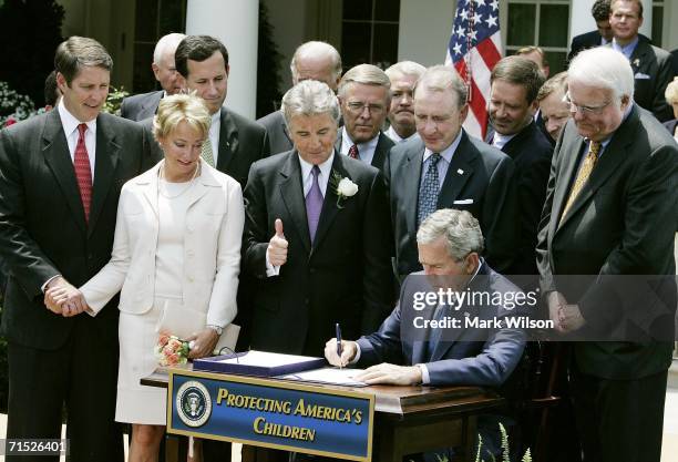 President George W. Bush signs the H.R. 4472, the Adam Walsh Child Protection and Safety Act of 2006, while John Walsh gives a thumbs up and his wife...