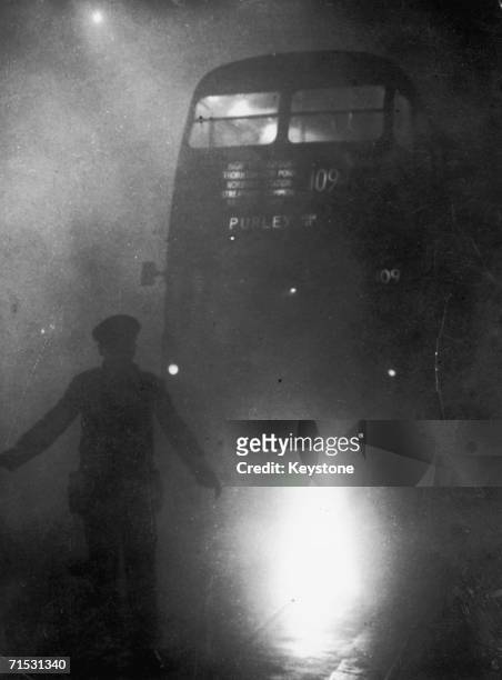 London bus conductor is forced to walk ahead of his vehicle to guide it through the smog, 9th December 1952.