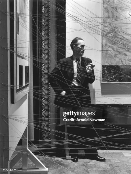 French-born artist Marcel Duchamp holds a pipe as he poses behind his art installation 'Sixteen Miles of String,' New York, New York, 1942.