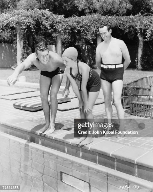 American silent era comedian Harold Lloyd looks on fondly as actor Buster Crabbe gives Lloyd's daughter a swimming lesson at his Beverly Hills...