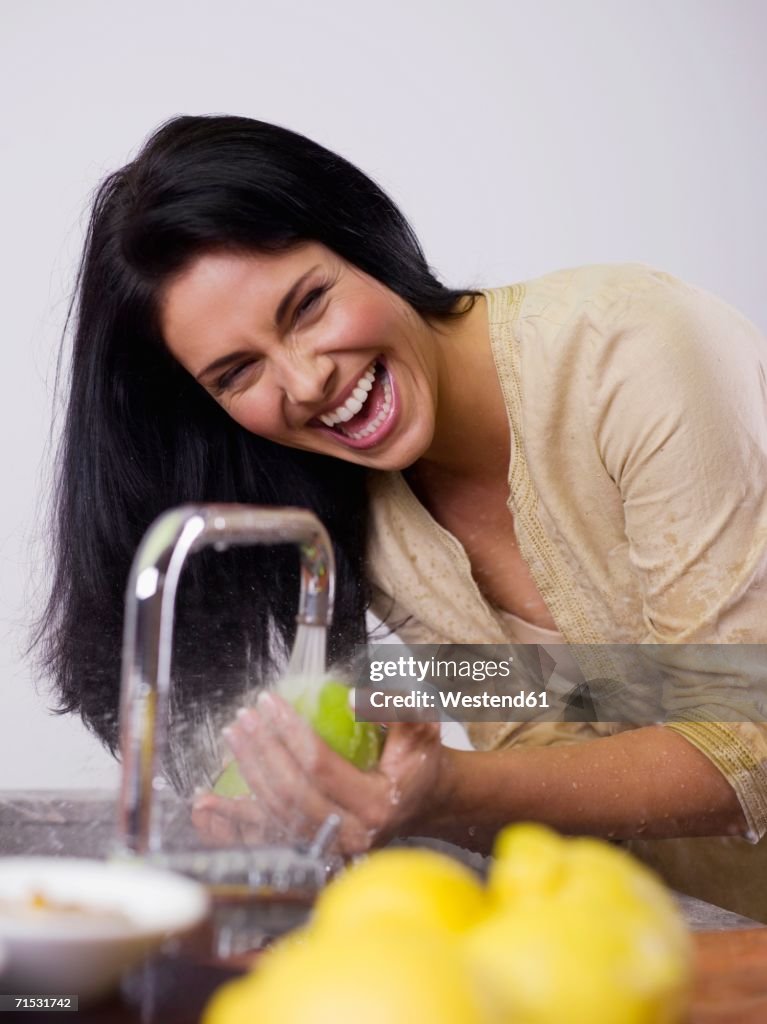 Woman washing fruit at kitchen sink, laughing