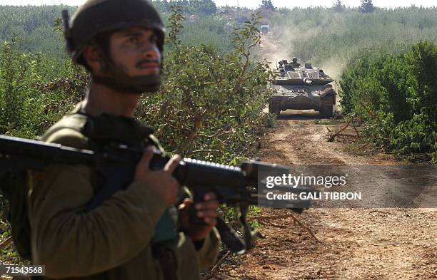 An Israeli soldier armed with an M-16 rifle secures the area as a tank makes its way to position along the northern Israeli border during shelling,...