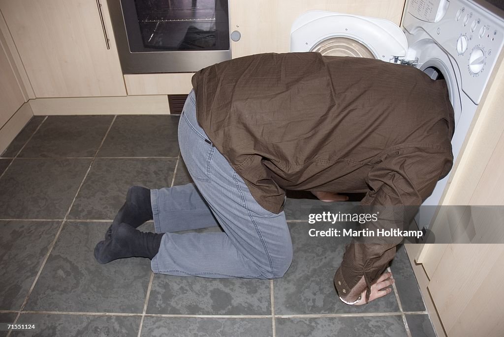 Man kneeling down with his head in a washing machine