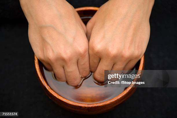 a woman soaking her fingers in a bowl in preparation for a manicure - fradicio foto e immagini stock