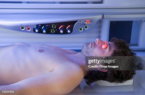 young man lying down in a tanning bed - tanning bed stock pictures, royalty-free photos & images