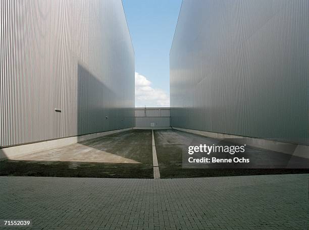 road between warehouse buildings leading to closed gate - marquage de route photos et images de collection