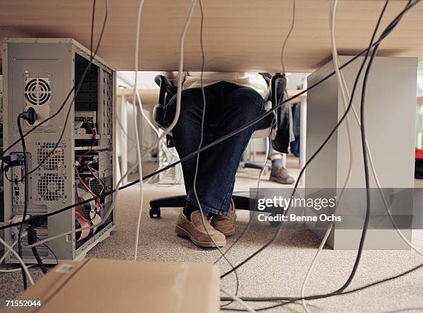 man sitting at desk and cables plugged into back of computer - cable mess stockfoto's en -beelden