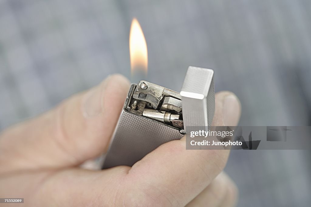 Person holding a lit cigarette lighter