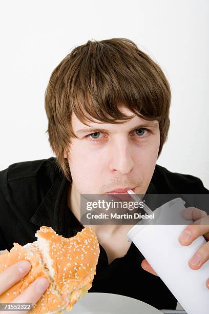 young man drinking soda and eating a burger - brot mund stock-fotos und bilder