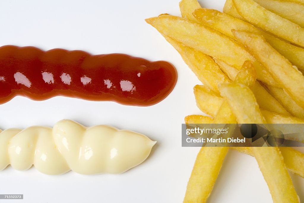 Pile of french fries next to blobs of ketchup and mayonnaise