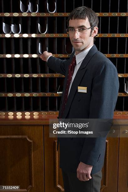 hotel clerk reaching for paper in pigeon hole - pigeon hole stock pictures, royalty-free photos & images
