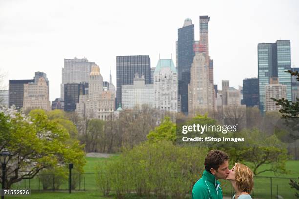 young couple kissing in central park with manhattan skyline in background, new york city - couple central park stock pictures, royalty-free photos & images