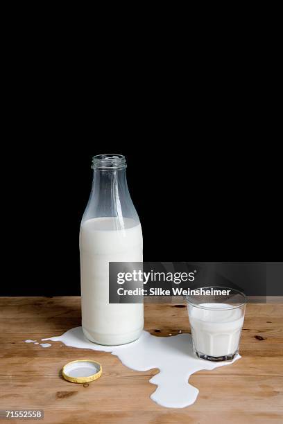 milk bottle and glass in puddle of spilt milk - spilt milk foto e immagini stock