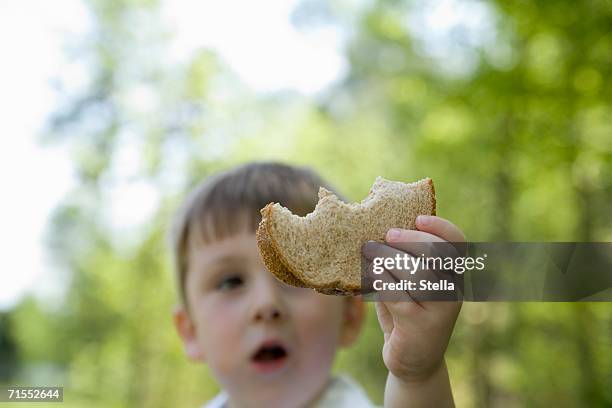 young boy standing in park and holding slice of bread - brot mund stock-fotos und bilder