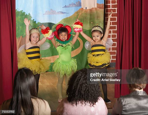 three young girls in bee and flower costumes on stage - girl stage stock-fotos und bilder