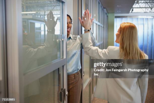 two female coworkers giving each other a high five - three quarter length stock pictures, royalty-free photos & images