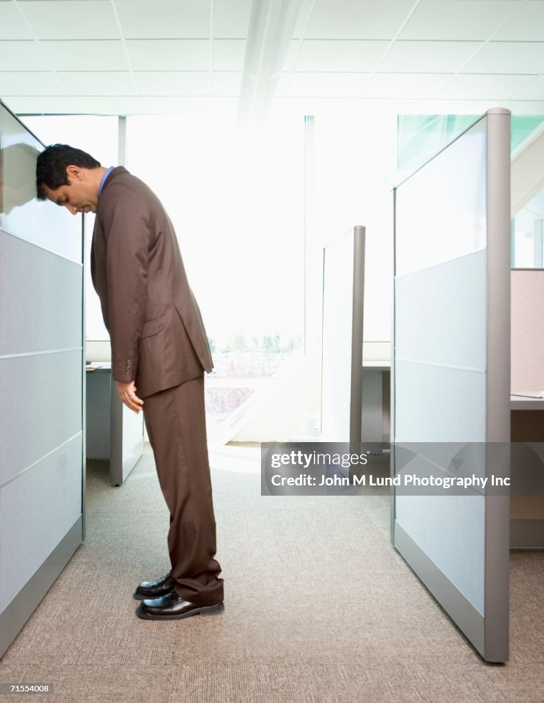 Businessman leaning head against office cubicle wall