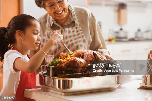 hispanic granddaughter helping grandmother baste turkey - thanksgiving stock pictures, royalty-free photos & images