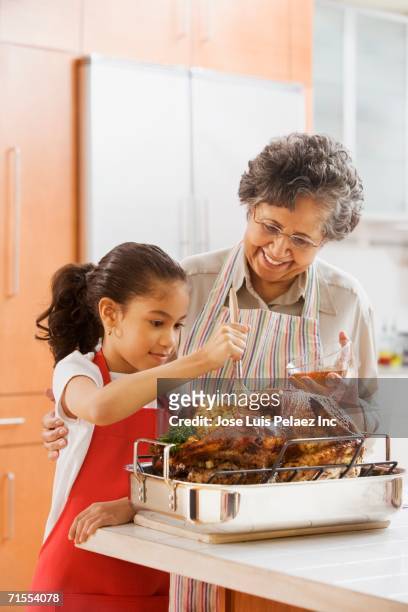 hispanic granddaughter helping grandmother baste turkey - bañar en su jugo durante la cocción fotografías e imágenes de stock