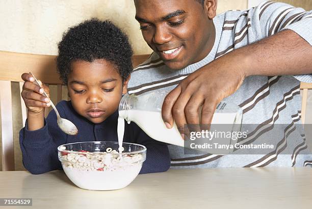 african american father pouring milk into young son's cereal - boy eating cereal stock pictures, royalty-free photos & images