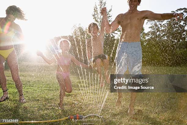 family playing in sprinkler - mom flirting stockfoto's en -beelden