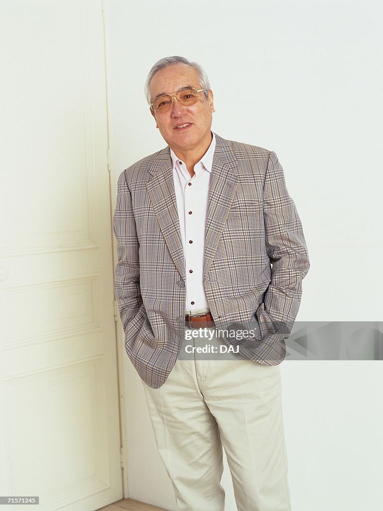 Senior man standing in front of white door with hands in his pocket, looking at camera, Smiling, Front View