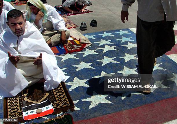 Shiite Iraqi performs Friday Prayers as another one walks over a drawing of US national flag ahead of a rally in Baghdad's poor neighborhood of Sadr...