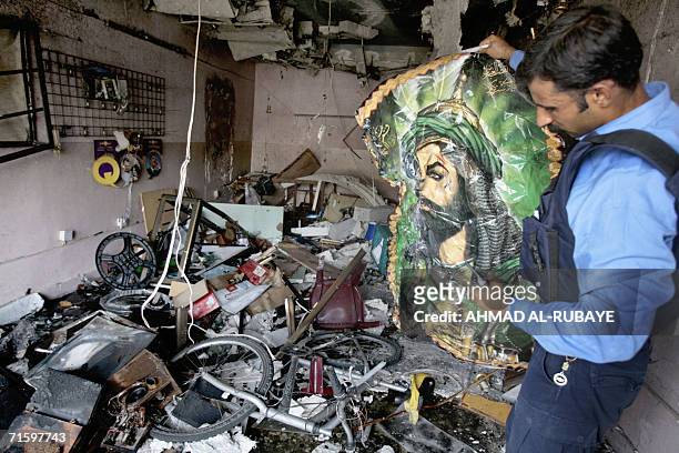 An Iraqi policeman removes a picture of Abu al-Fadl al-Abbas, son of revered Shiite Imam Ali, from the rubble inside a shop at the site 07 August...